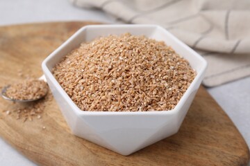 Dry wheat groats in bowl on light table, closeup