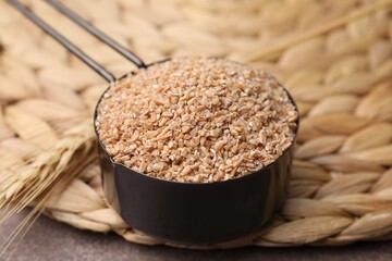 Dry wheat groats in scoop and spikelet on table, closeup