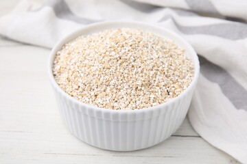 Dry barley groats in bowl on white wooden table, closeup