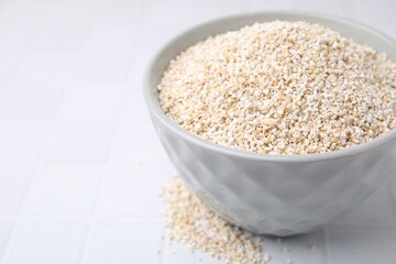 Dry barley groats in bowl on white tiled table, closeup. Space for text