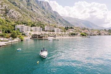 Small yacht is moored in the sea against the backdrop of a hotel complex. Dobrota, Montenegro