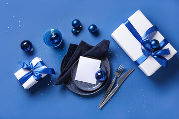 Beautiful table setting for Christmas dinner with gifts and decorations on blue background