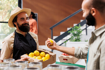 Smiling customer admiring fresh lemon picked from the box held by caucasian vendor. Friendly...