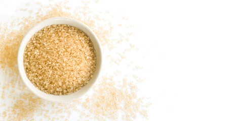 Small bowl of raw brown sugar with scattered crystals on white background