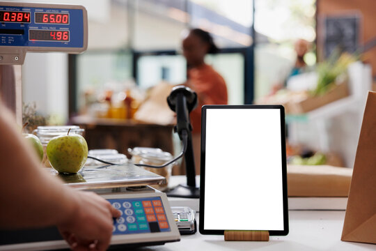 Close-up Of Digital Device Displaying Isolated Mockup Template Is Seen At An Eco-friendly Food Store. Phone Tablet With An Empty Mockup Display, Placed Near Electronic Measuring Scale Used By Vendor.