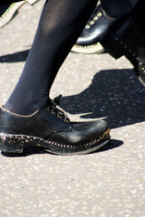 dancing feet in black shoes and clogs and black stockings on a tarmac pavement