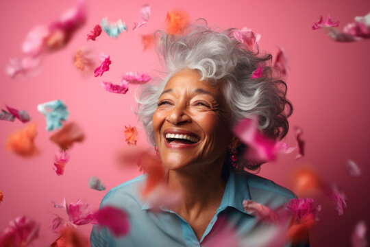 Close-up portrait of cheerful senior grey-haired woman with colorful confetti on pink background.