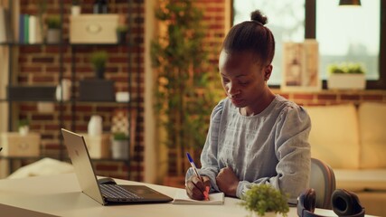 Freelancer taking notes about work, using notebook planner to help with remote job productivity at...