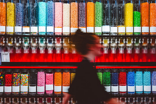 A woman walks past a wall of candy dispensers, motion blurred