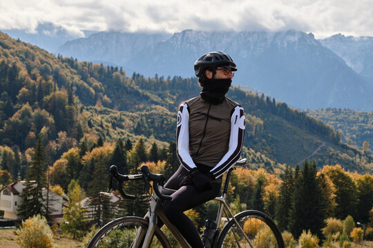 Close-up photo of man cyclist wearing full cycling winter kit and helmet. Man cyclist standing against autumn mountains background. Cyclist riding gravel bike. Gravel biking adventure in mountains.