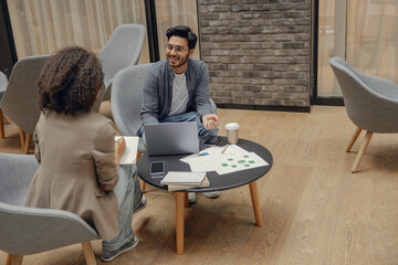 Woman office worker writing something down while sitting with colleague in modern office 