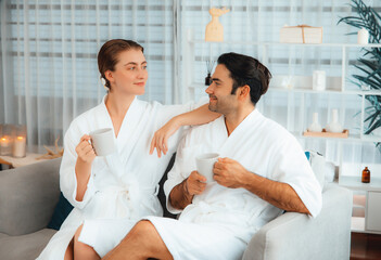 Obraz na płótnie Canvas Beauty or body treatment spa salon vacation lifestyle concept with couple wearing bathrobe relaxing with drinks in luxurious hotel spa or resort room. Vacation and leisure relaxation. Quiescent