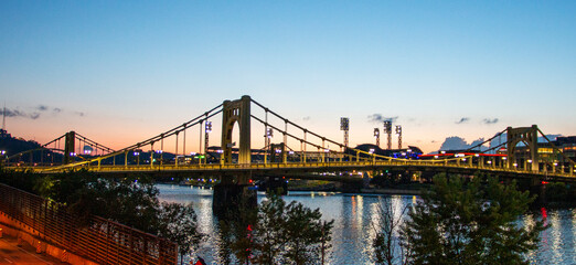 A Majestic Bridge Connecting the Cityscape to Nature's Serene Waterfront at dusk in Pittsburgh - obrazy, fototapety, plakaty
