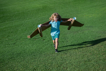 Child boy playing with cardboard toy airplane wings craft in sky with copy space for text. Creative...