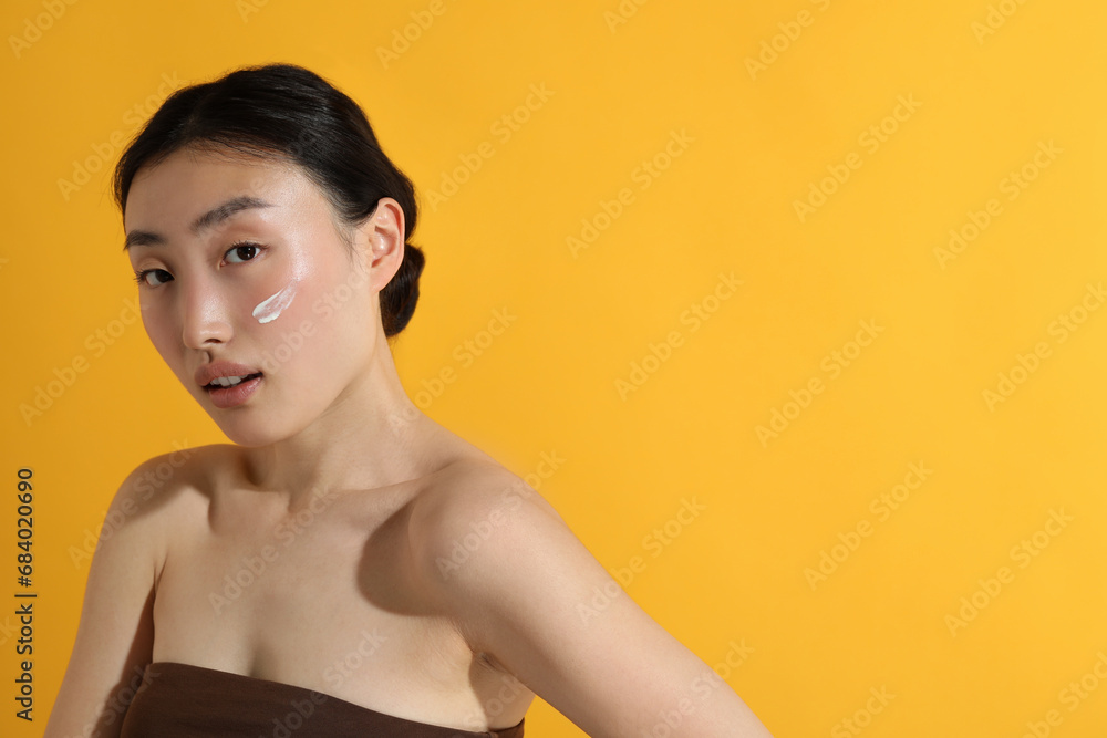 Canvas Prints Beautiful young woman with sun protection cream on her face against orange background, space for text