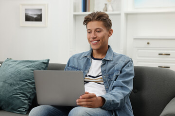 Happy young man having video chat via laptop on sofa indoors