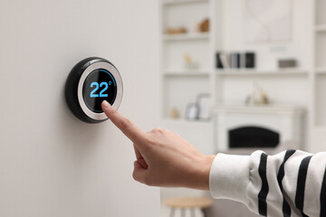 Smart home system. Woman using thermostat indoors, closeup