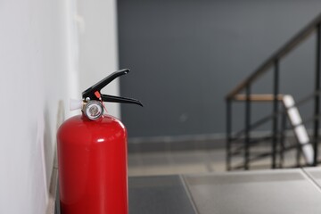 Red fire extinguisher near white wall, space for text