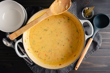 Homemade German Potato Soup (Kartoffelsuppe) in a Dutch Oven: Creamy vegetable soup in a cast-iron pot with soup bowls and spoons on the side
