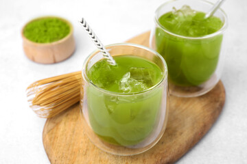 Delicious iced green matcha tea and bamboo whisk on white table, closeup