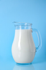 Jug of fresh milk on light blue background