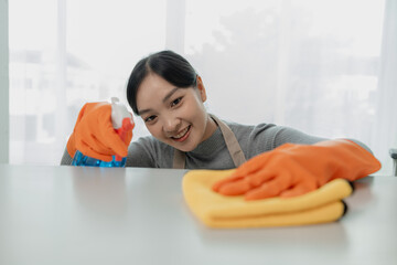 Obraz na płótnie Canvas Asian female cleaner wiping down tables with cleaning spray, the housekeeper is cleaning the work desk for hygiene because of the Covid-19, cleaning idea.