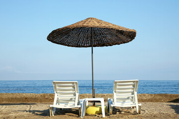 Two lounge chairs and beach umbrella on sea shore