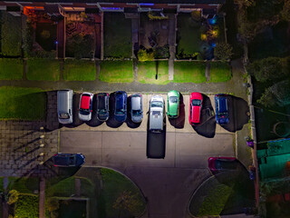 Aerial night view of a parking lot illuminated by street lights, featuring nine cars parked in...