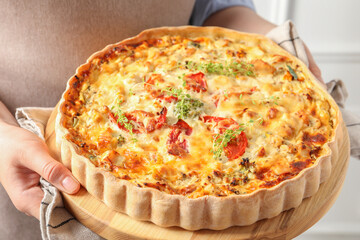 Woman holding board with tasty quiche indoors, closeup