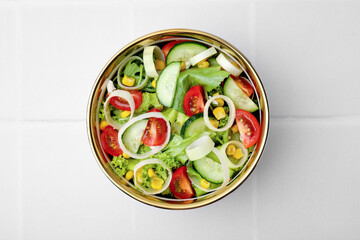 Bowl of tasty salad with leek, tomatoes and cucumbers on white tiled table, top view