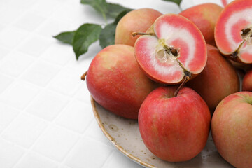 Fototapeta na wymiar Tasty apples with red pulp and leaves on white tiled table, closeup. Space for text