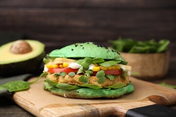 Tasty green vegan burger with vegetables, patty and microgreens on wooden table, closeup