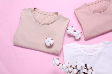 Cotton branch with fluffy flowers and t-shirts on pink background, flat lay