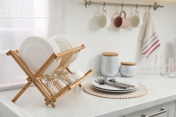 Fototapeta na wymiar Drying rack with clean dishes on light marble countertop in kitchen
