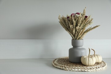 Beautiful bouquet of dry flowers and small pumpkins on white table near light wall, space for text