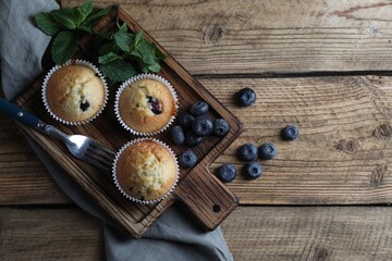 Delicious sweet muffins with blueberries, mint and fork on wooden table, flat lay. Space for text