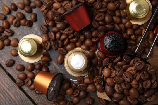 Saucepan with coffee capsules and beans on wooden table, flat lay