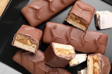 Tasty chocolate bars with nougat and nuts on black plate, top view