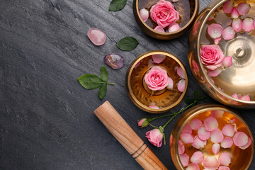 Tibetan singing bowls with water, beautiful rose flowers and mallet on gray table, flat lay. Space...