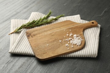 Wooden cutting board, kitchen towel, rosemary and salt on dark grey table