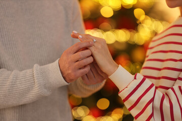 Making proposal. Man putting engagement ring on his girlfriend's finger against blurred lights,...