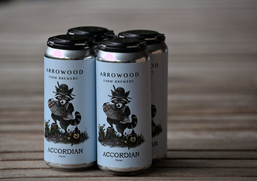 Four pack of Arrowood Farm Brewing Accordian Pilsner craft beer pint cans on a wooden table.