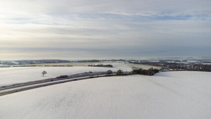 Aerial view of the picturesque English countryside blanketed in snow during winter. The drone captures the serene beauty of snow-covered fields, with the intricate patterns of the landscape highlighte