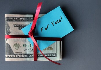 Cash Dollars money on gray background with red gift ribbon and a blue note written FOR YOU! -...