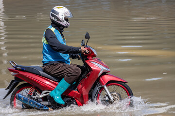 A taxi driver on a motorcycle drives through a flooded street, Bangkok, Thailand