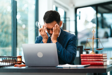 Asian male business lawyer looks stressed, pinching the bridge of his nose in front of a laptop at...