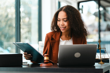Attractive smiling African American female lawyer reads a document in an office, with a laptop,...