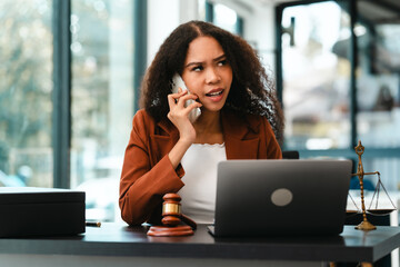 Attractive smiling African American female lawyer reads a document in an office, with a laptop, gavel, and scales of justice nearby, legal, legislation.