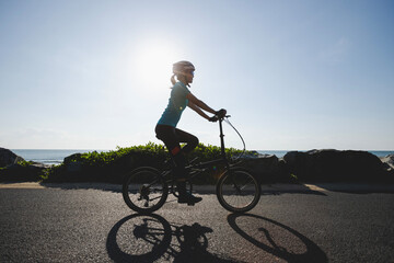 Riding folding bike on sunrise seaside road