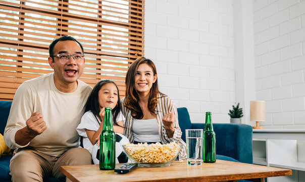 In their cozy living room, a joyful family of fans bond over a football match on TV, celebrating their team's success with cheers and excitement. The room is filled with togetherness and happiness.